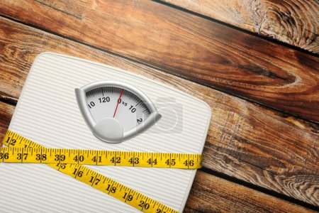 Photo for Weigh scales tied with measuring tape on wooden table, top view and space for text. Overweight concept - Royalty Free Image