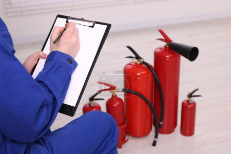 Photo for Man with clipboard checking fire extinguishers indoors, closeup - Royalty Free Image