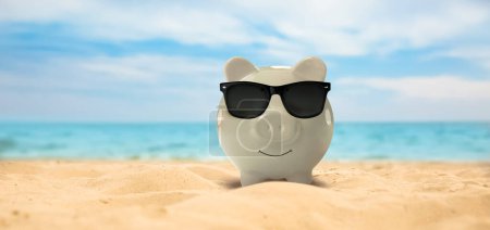 Photo for Vacation savings. Piggy bank with sunglasses on sandy beach near sea, banner design - Royalty Free Image