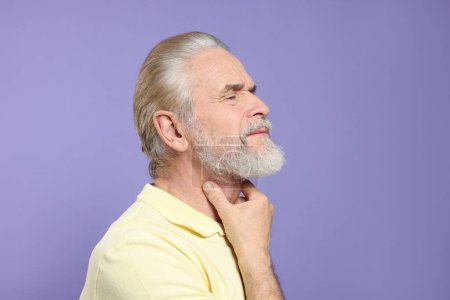 Téléchargez les photos : Homme âgé souffrant de maux de gorge sur fond violet clair. Symptômes de froid - en image libre de droit