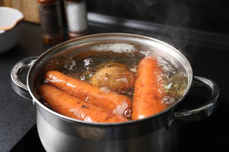 Boiling carrot and potatoes in pot on electric stove, closeup. Cooking vinaigrette salad