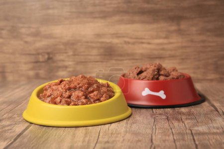 Wet pet food in feeding bowls on wooden floor