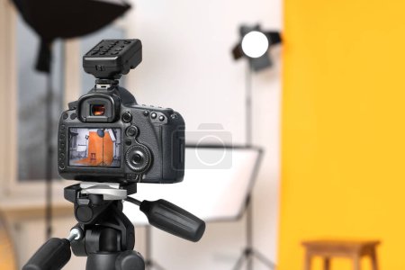 Foto de Trípode con cámara, taburete de bar y equipo de iluminación profesional en estudio fotográfico moderno, enfoque en la pantalla. Espacio para texto - Imagen libre de derechos