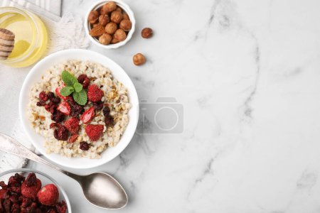 Photo for Oatmeal with freeze dried strawberries and mint served with honey and hazelnuts on white marble table, flat lay. Space for text - Royalty Free Image
