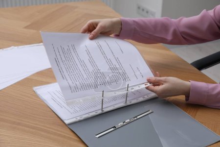 Woman putting punched pocket with document into folder at wooden table, closeup