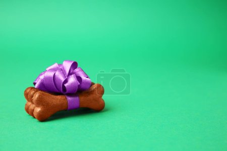 Téléchargez les photos : Cookies pour chien en forme d'os avec noeud violet sur fond vert, espace pour le texte - en image libre de droit