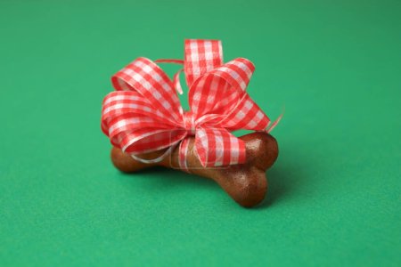 Téléchargez les photos : Cookie chien en forme d'os avec noeud rouge sur fond vert, gros plan - en image libre de droit