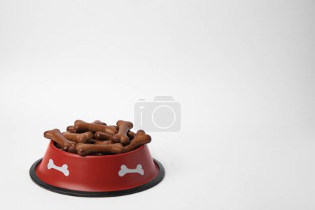 Téléchargez les photos : Bol rouge avec biscuits pour chien en forme d'os sur fond blanc, espace pour le texte - en image libre de droit