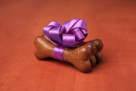 Téléchargez les photos : Cookies pour chien en forme d'os avec noeud violet sur fond en bois, gros plan - en image libre de droit