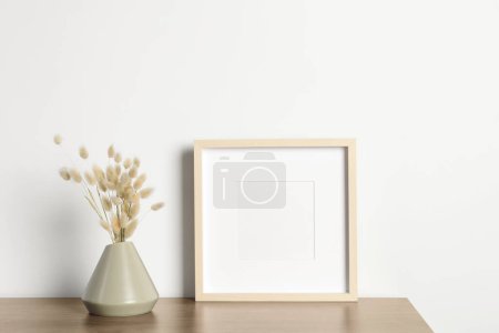Leerer Fotorahmen und Vase mit trockenen Ziernägeln auf Holztisch. Mockup für Design