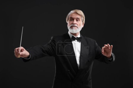 Professional conductor with baton on black background