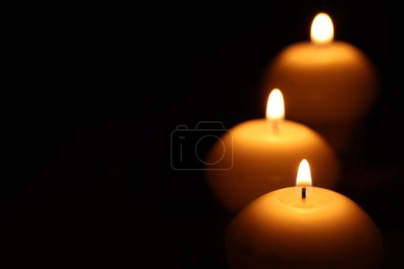 Burning wax candles on black background, closeup. Space for text