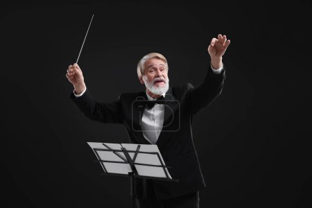 Foto de Conductor profesional con bastón y soporte de notas sobre fondo negro - Imagen libre de derechos