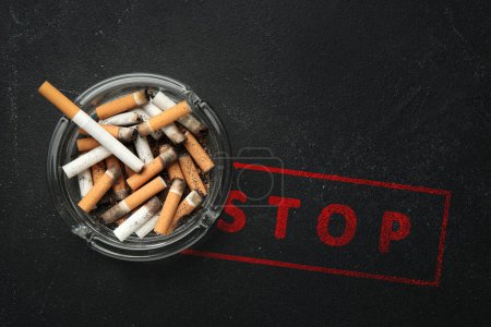 Photo for Quit smoking. Glass ashtray with stubs and word Stop on black table, top view - Royalty Free Image