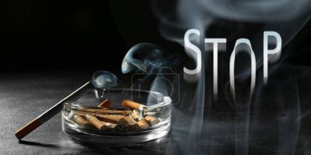 Photo for Quit smoking. Word Stop of smoke, ashtray with stubs and smoldering cigarette on table against black background, banner design - Royalty Free Image