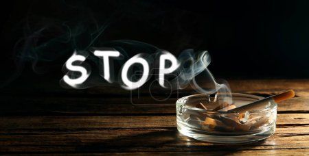 Photo for Quit smoking. Word Stop of smoke, ashtray with stubs and smoldering cigarette on wooden table against black background, banner design - Royalty Free Image