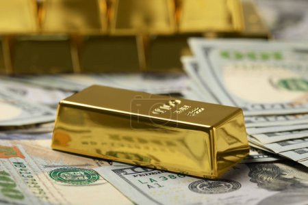 Shiny gold bar on dollar banknotes, closeup