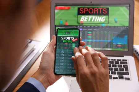Photo for Man betting on sports using smartphone and laptop at table, closeup. Bookmaker websites on displays - Royalty Free Image