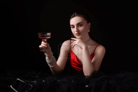 Foto de La foto a la moda de la joven atractiva con la copa del vino sobre el fondo negro - Imagen libre de derechos