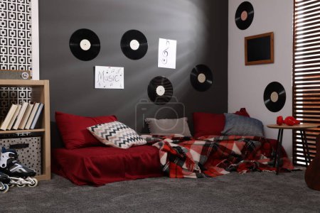 Foto de Elegante habitación de adolescente con cama, mesa de madera y discos de vinilo en la pared. Diseño de interiores - Imagen libre de derechos