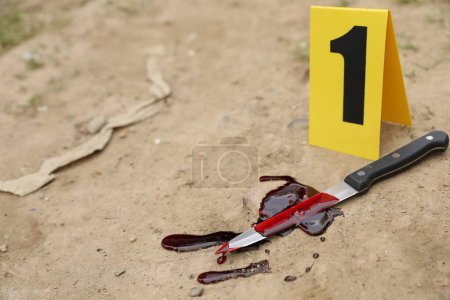Photo for Crime scene marker and bloody knife on ground outdoors. Space for text - Royalty Free Image