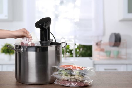 Photo for Woman putting vacuum packed meat into pot with sous vide cooker on wooden table in kitchen, closeup. Thermal immersion circulator - Royalty Free Image