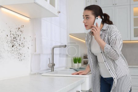 Photo for Mold removal service. Woman talking on phone and looking at affected wall in kitchen - Royalty Free Image
