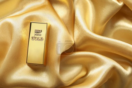 Barra de oro en tela de seda brillante, vista superior. Espacio para texto