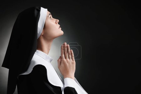 Monja con las manos cerradas rezando a Dios sobre fondo negro. Espacio para texto