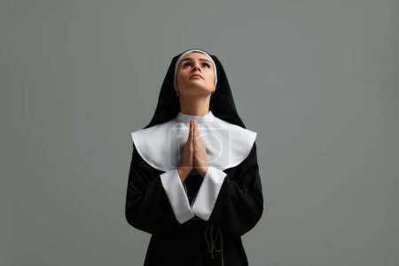 Téléchargez les photos : Nonne avec les mains jointes priant Dieu sur fond gris - en image libre de droit