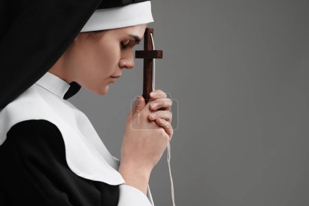 Téléchargez les photos : Nonne avec croix priant Dieu sur fond gris. Espace pour le texte - en image libre de droit