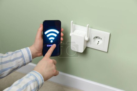 Photo for Woman with smartphone connecting to internet via wireless repeater indoors, closeup. Wi-Fi symbol on device screen - Royalty Free Image