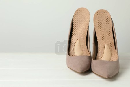 Orthopedic insoles in high heel shoes on white wooden floor, closeup. Space for text