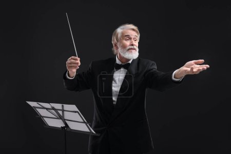 Foto de Conductor profesional con bastón y soporte de notas sobre fondo negro - Imagen libre de derechos
