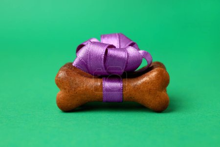 Téléchargez les photos : Cookies pour chien en forme d'os avec noeud violet sur fond vert, gros plan - en image libre de droit