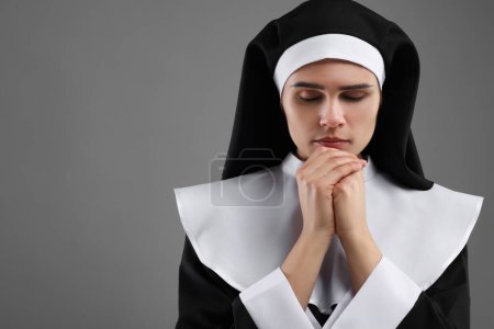 Nonne avec les mains jointes priant Dieu sur fond gris. Espace pour le texte