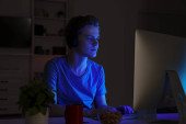 Teenage boy using computer in bedroom at night. Internet addiction Poster #658402644