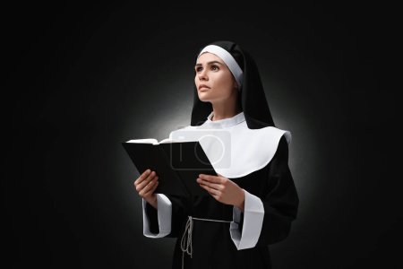 Téléchargez les photos : Jeune religieuse avec Bible sur fond noir - en image libre de droit