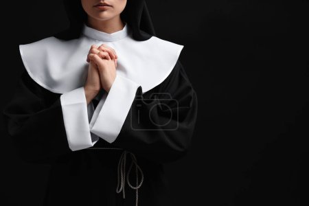 Téléchargez les photos : Nonne avec les mains jointes priant Dieu sur fond noir, gros plan. Espace pour le texte - en image libre de droit