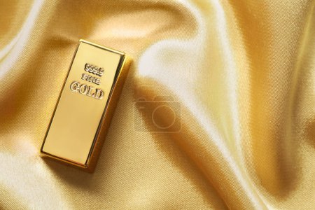 Gold bar on shiny silk fabric, top view. Space for text