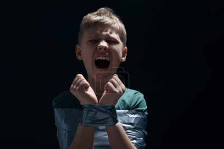 Photo for Scarred little boy tied up and taken hostage on dark background. Space for text - Royalty Free Image