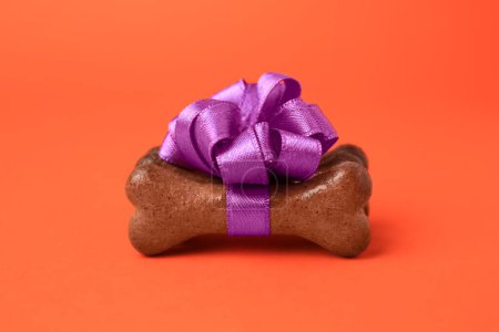Téléchargez les photos : Cookies pour chien en forme d'os avec noeud violet sur fond orange, gros plan - en image libre de droit