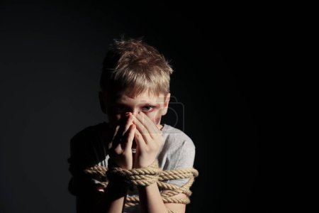 Photo for Little boy with bruises tied up and taken hostage on dark background. Space for text - Royalty Free Image