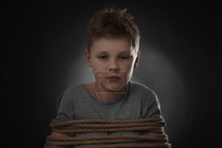 Photo for Little boy tied up and taken hostage on dark background - Royalty Free Image