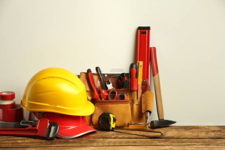 Foto de Cinturón de cuero con herramientas para la reparación y sombreros duros en mesa de madera - Imagen libre de derechos