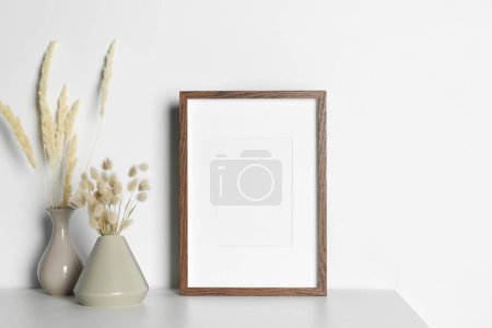 Photo for Empty photo frame and vases with dry decorative spikes on white table. Mockup for design - Royalty Free Image