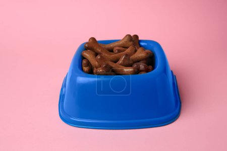 Téléchargez les photos : Bol bleu avec biscuits pour chien en forme d'os sur fond rose - en image libre de droit