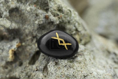 Black rune Inguz on stone outdoors, closeup