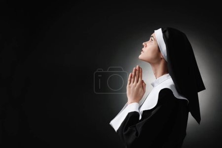 Téléchargez les photos : Nonne avec les mains jointes priant Dieu sur fond noir. Espace pour le texte - en image libre de droit