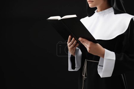 Nun reading Bible on black background, closeup. Space for text